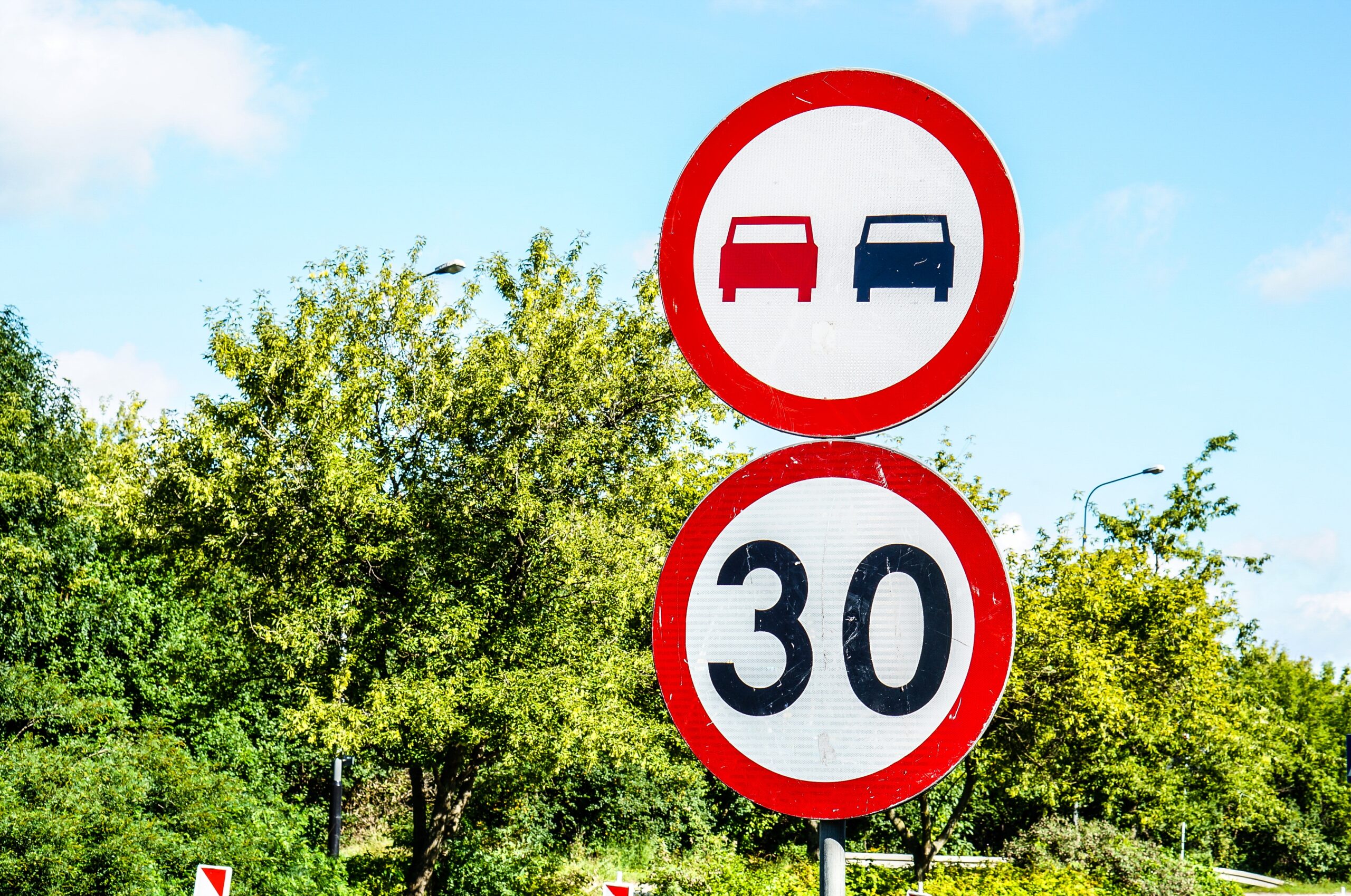 Sign indicating speed limit of thirty and no overtaking against green trees A sign indicating speed limit of thirty and no overtaking against green trees