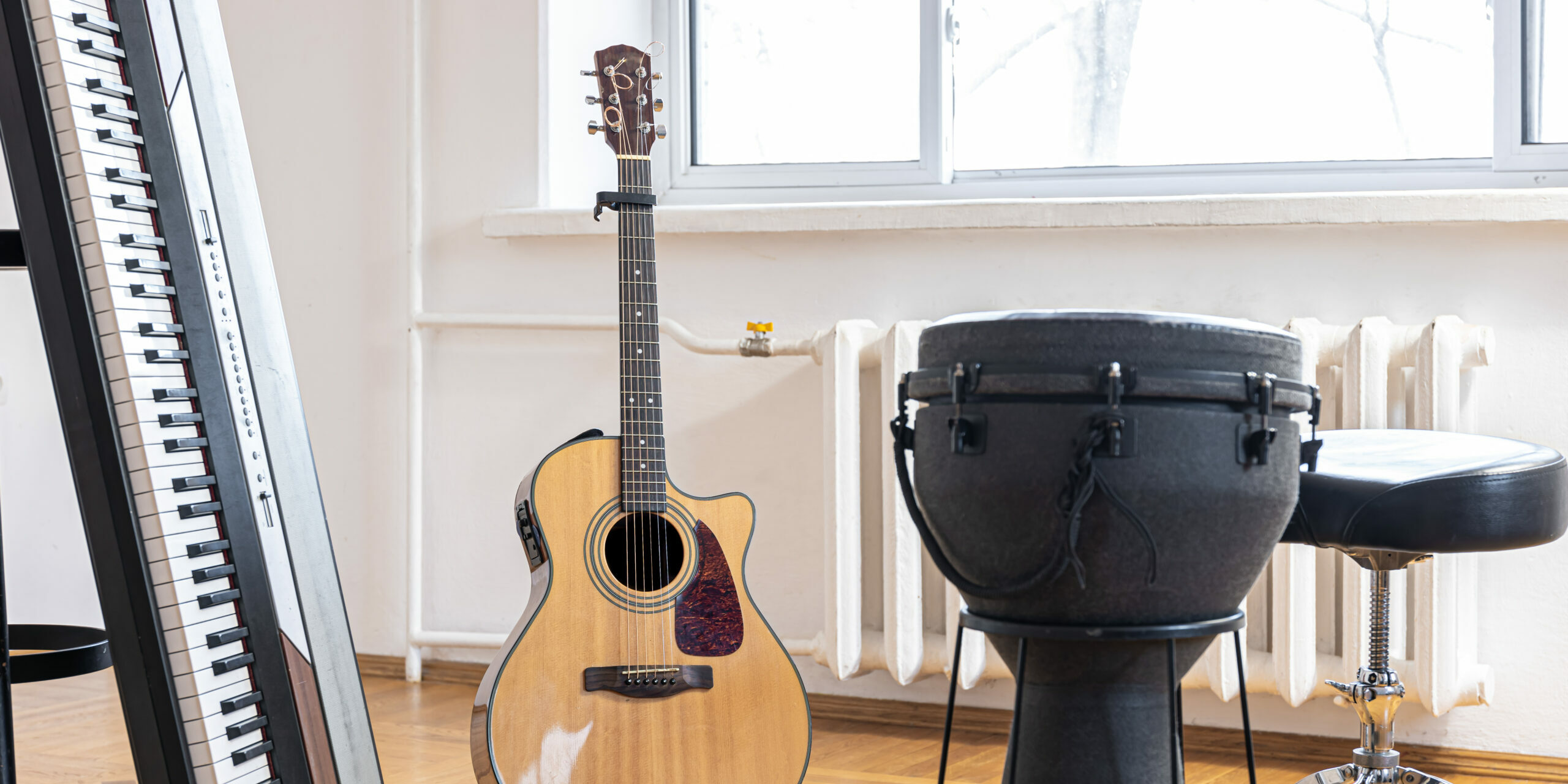 Musical keys and acoustic guitar on a stand in an empty light room, blurred background.